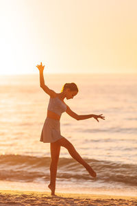Side view of woman jumping at beach against sky during sunset