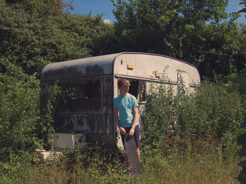 Man looking away while holding skateboard against travel trailer during sunny day