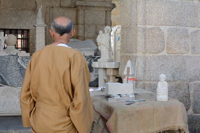 Rear view of craftsperson in front of statues on table at workshop