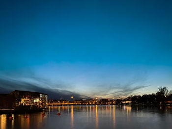 Illuminated buildings by sea against sky at dusk