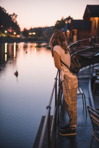 Rear view of woman standing by sea against sky during sunset