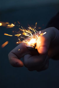 Cropped hand holding cigarette lighter with sparks at night