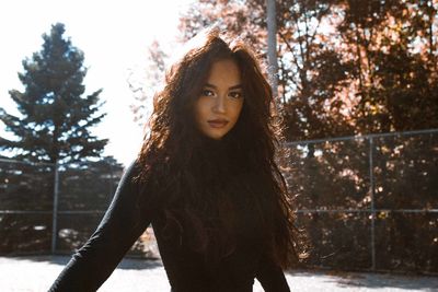 Portrait of young woman standing against trees against sky