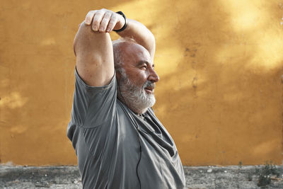 An older man with white hair and beard is stretching his arm