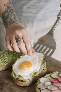 Woman garnishing omelet on guacamole spread bread while standing at kitchen