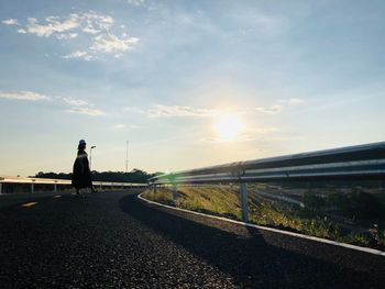 Rear view of man standing on road against sky during sunset