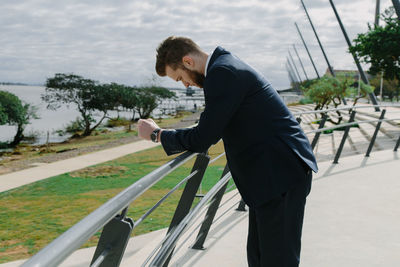 Businessman standing at railing against sky