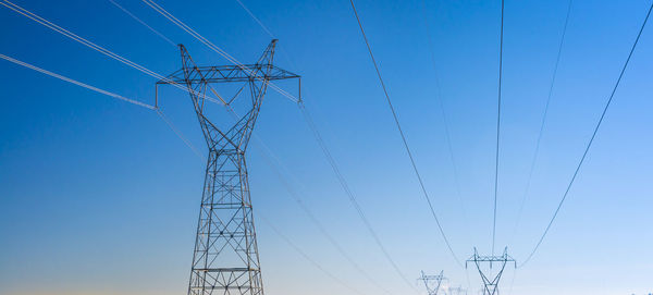 Low angle view of electricity pylon against blue sky