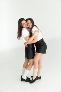 Two beautiful women twin sisters having fun together, posing white background, full length portrait