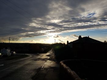 Road by buildings against sky at sunset