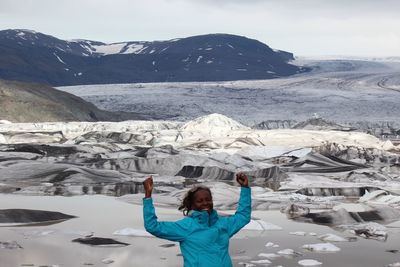 Mature woman with arms raised standing against glacier