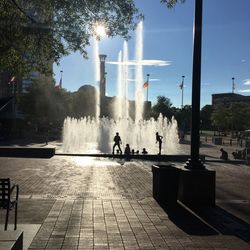 People on fountain in city against sky