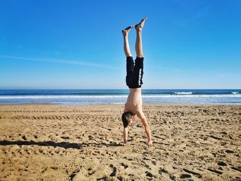 Woman with arms raised on beach against sky