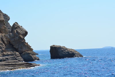 Rocks in sea against clear blue sky