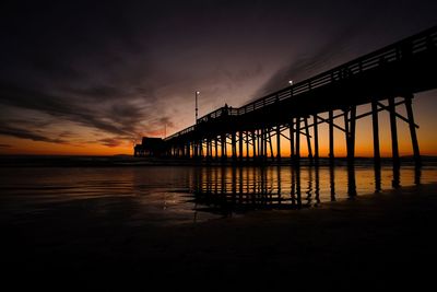 Silhouette bridge over sea against sky at sunset