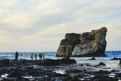 People standing on cliff by sea against sky