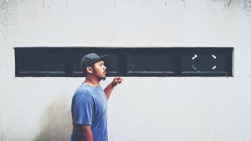 Side view of young man looking away while standing by wall