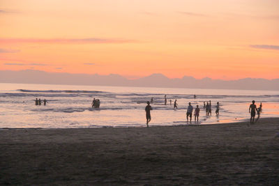 Silhouette people on beach against sky during sunset