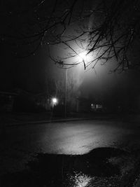 Illuminated road by trees against sky at night