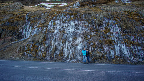 Portrait of couple standing by road against rock formation during winter