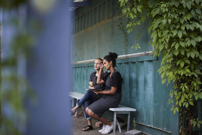 Gardeners looking away while sitting on bench at yard