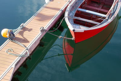 Small red wooden boat moored on dock and reflected on the water