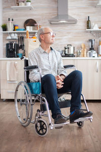 Full length of man sitting on wheelchair at home