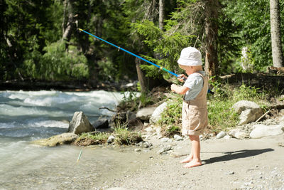 Little child boy fishing with a fishing rod on the mountain river on summer day