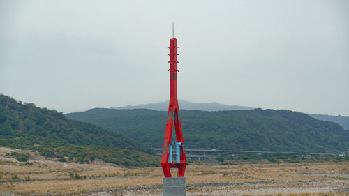 Red telephone pole on field against sky