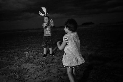 Siblings playing with ball on field at dusk