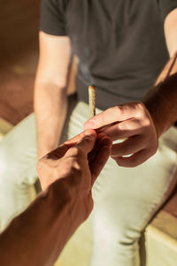 Cropped hand giving marijuana joint to man outdoors