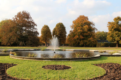 Fountain in park by lake against sky