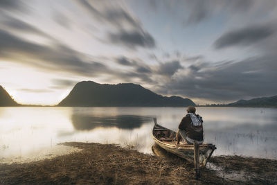 Man sitting on boat in lake against sky