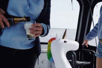 Midsection of woman pouring champagne in glass while standing with friend in yacht