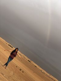 Full length of young woman standing on sand against sky