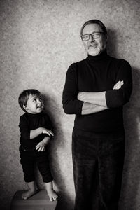 Grandfather with beard and glasses stands with his grandson in the studio near the wall