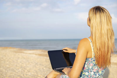 Rear view of woman using mobile phone at beach