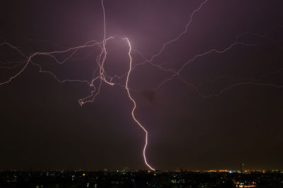 Lightning over cityscape against sky at night