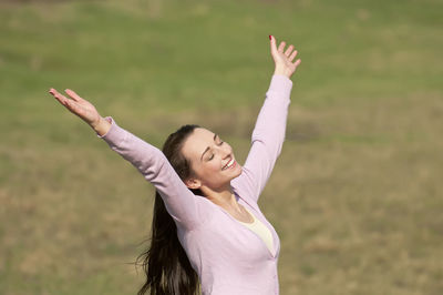 High angle view of smiling mid adult woman with arms raised standing on grassy field in park