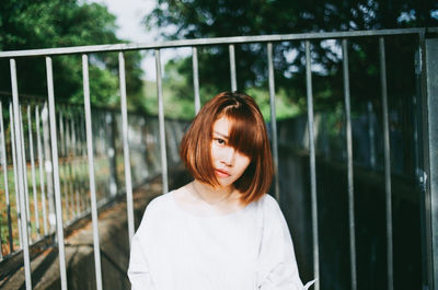 Portrait of woman standing against railing in park