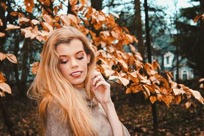 Smiling young woman by autumn leaves in park