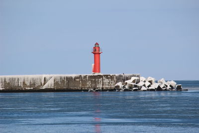 Lighthouse by sea against clear sky