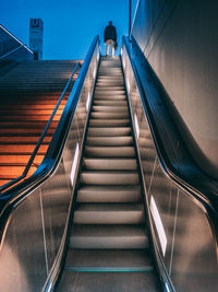 Low angle view of man standing on escalator at dusk