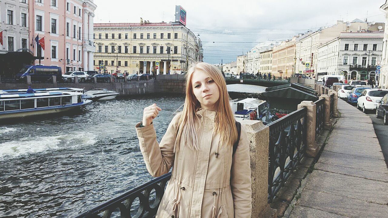 building exterior, lifestyles, built structure, architecture, leisure activity, transportation, water, person, young adult, casual clothing, mode of transport, looking at camera, railing, city, canal, incidental people, young women, sitting