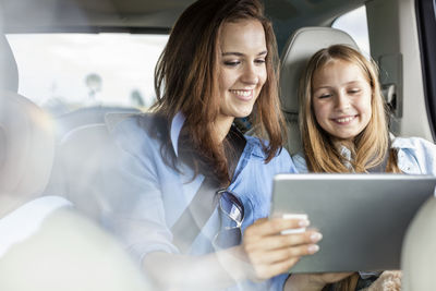 Mother and daughter on road trip sitting in car looking at digital tablet