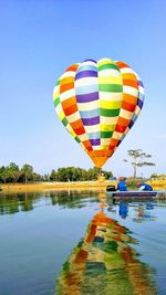 Multi colored hot air balloon flying over lake against sky