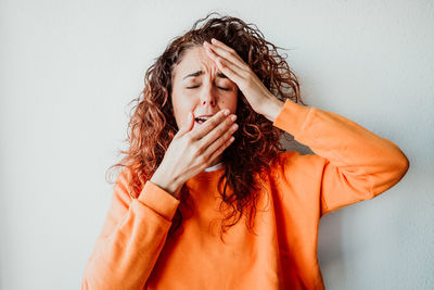 Woman sneezing while standing against wall