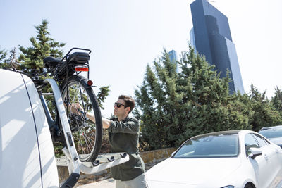 Side view of male putting modern bike on metal rack installed on automobile parked in city