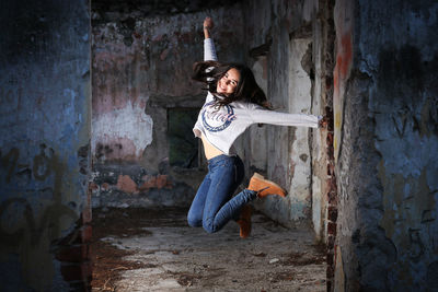 Portrait of young woman jumping at abandoned building