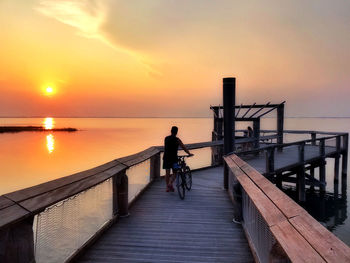 Man on pier over sea against sky during sunset